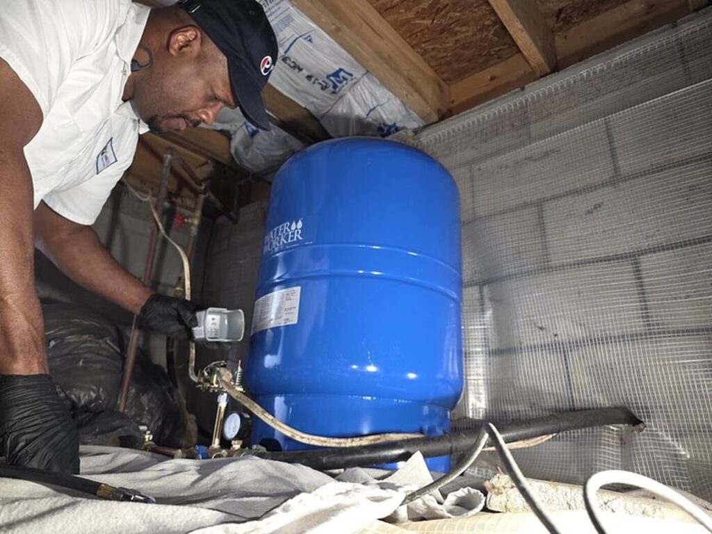 Plumbifi technician installing a blue well pressure tank and copper supply lines in a home crawl space